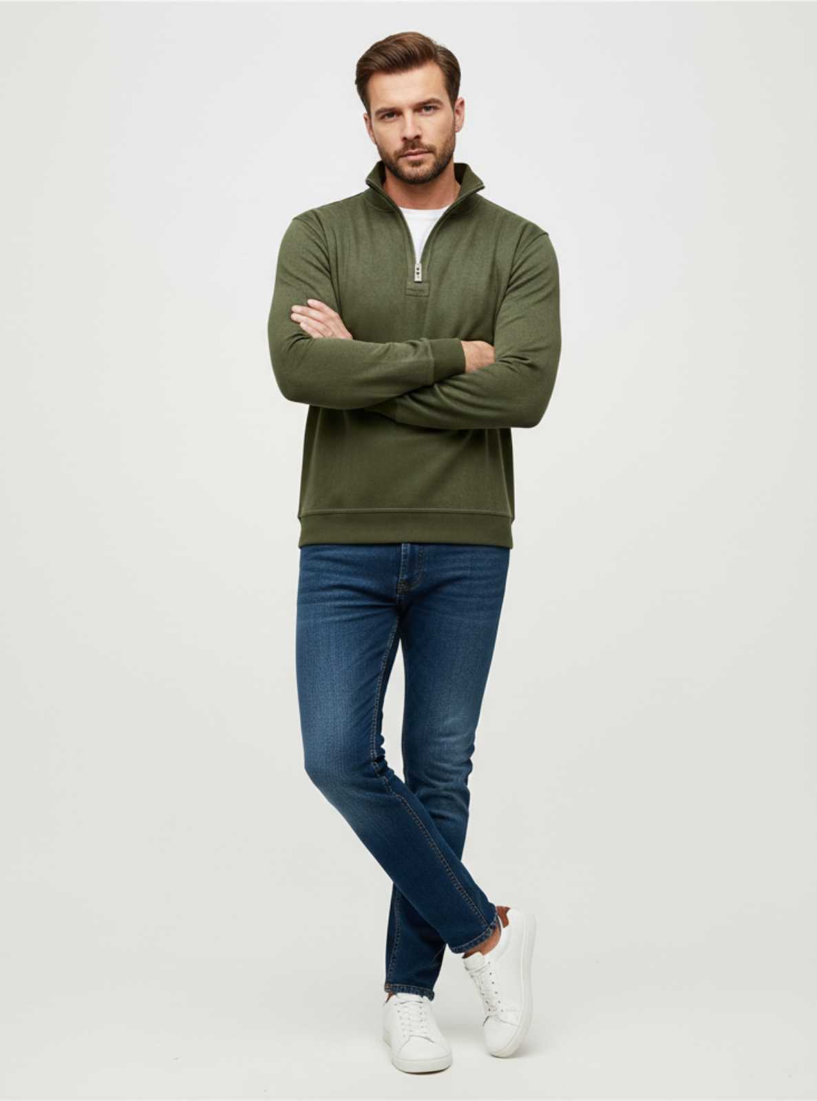 Man wearing a green half-zip sweater and blue jeans on a white background