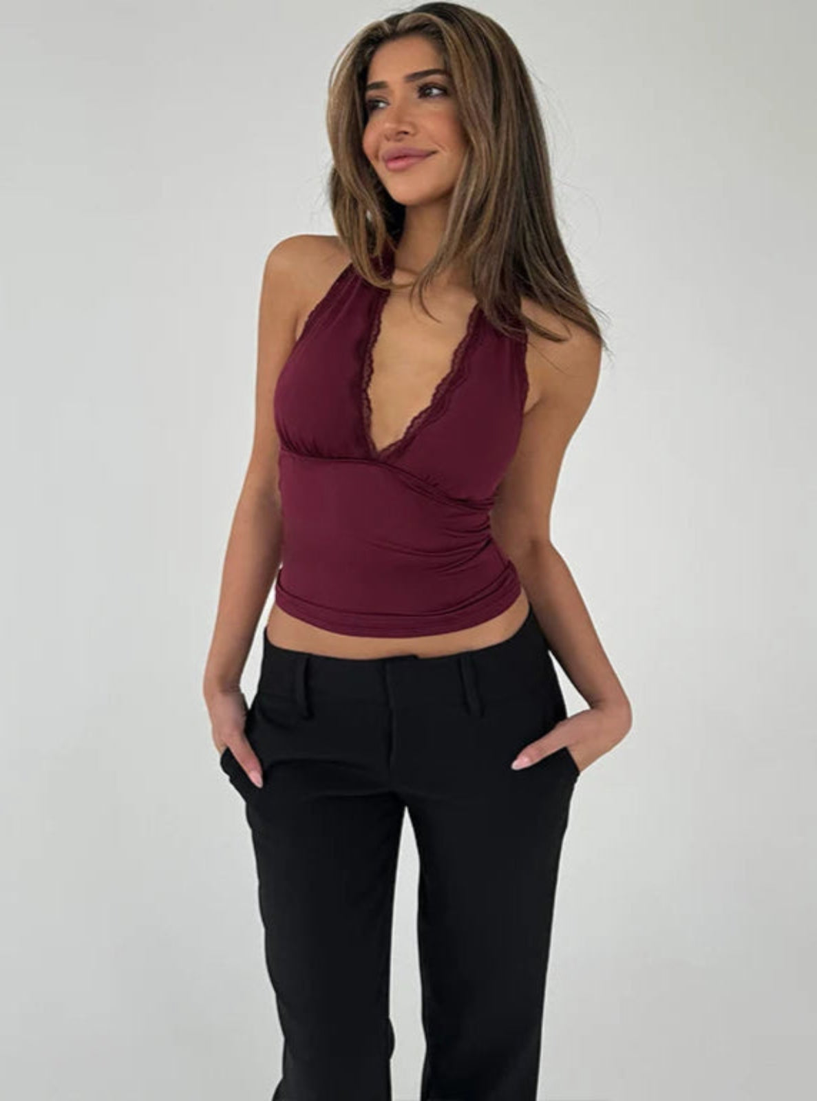 Woman wearing a burgundy halter top and black pants on a plain background