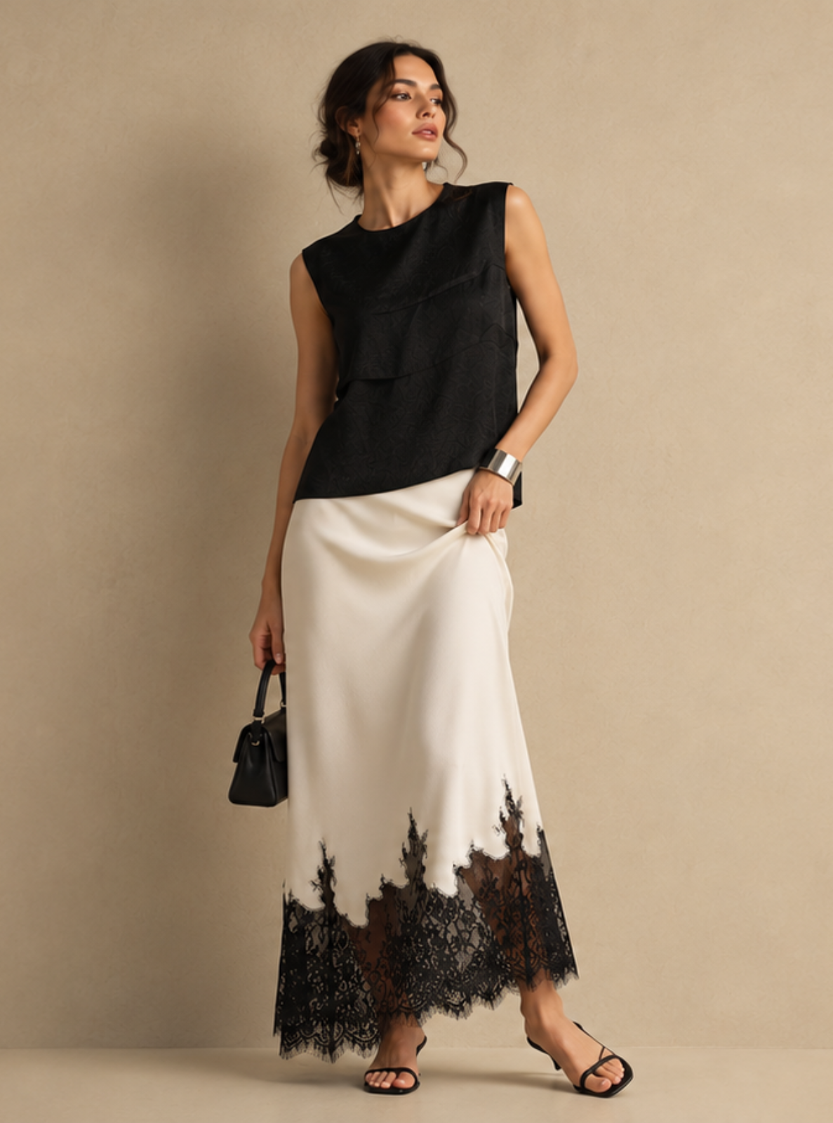 A woman models a sleeveless black top and a long white skirt with a black lace hem, standing against a plain beige studio background.