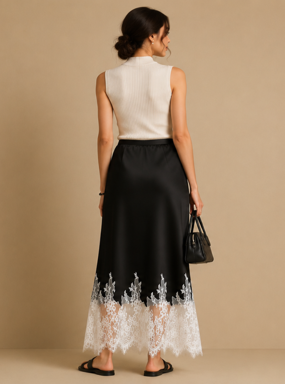 A woman stands with her back to the camera wearing a sleeveless white top and a black midi skirt with white lace trim at the hem, holding a black handbag against a plain beige studio background.