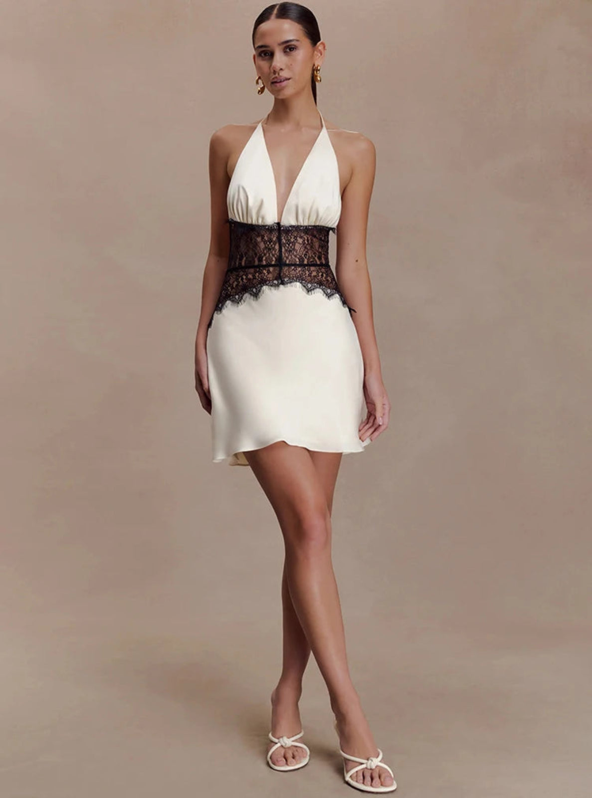 Woman wearing a white dress with black lace details on a beige background