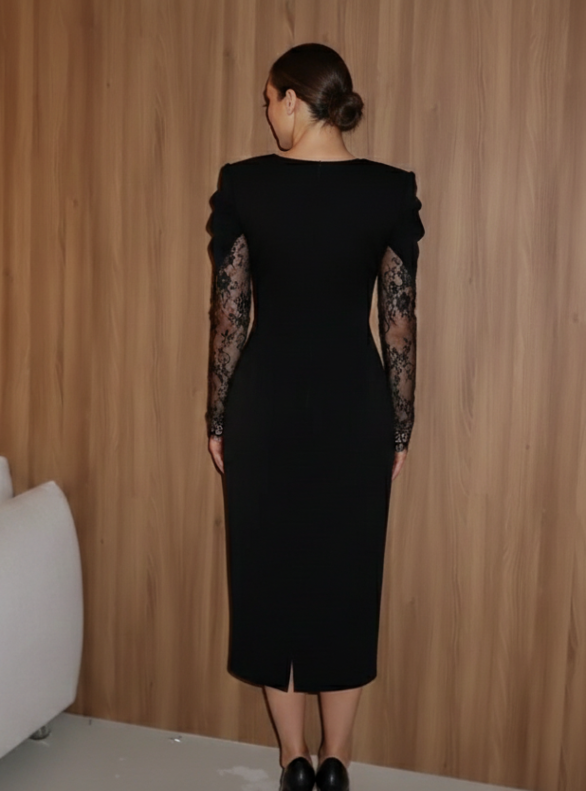 Woman in a black dress standing against a wooden wall with a white couch.