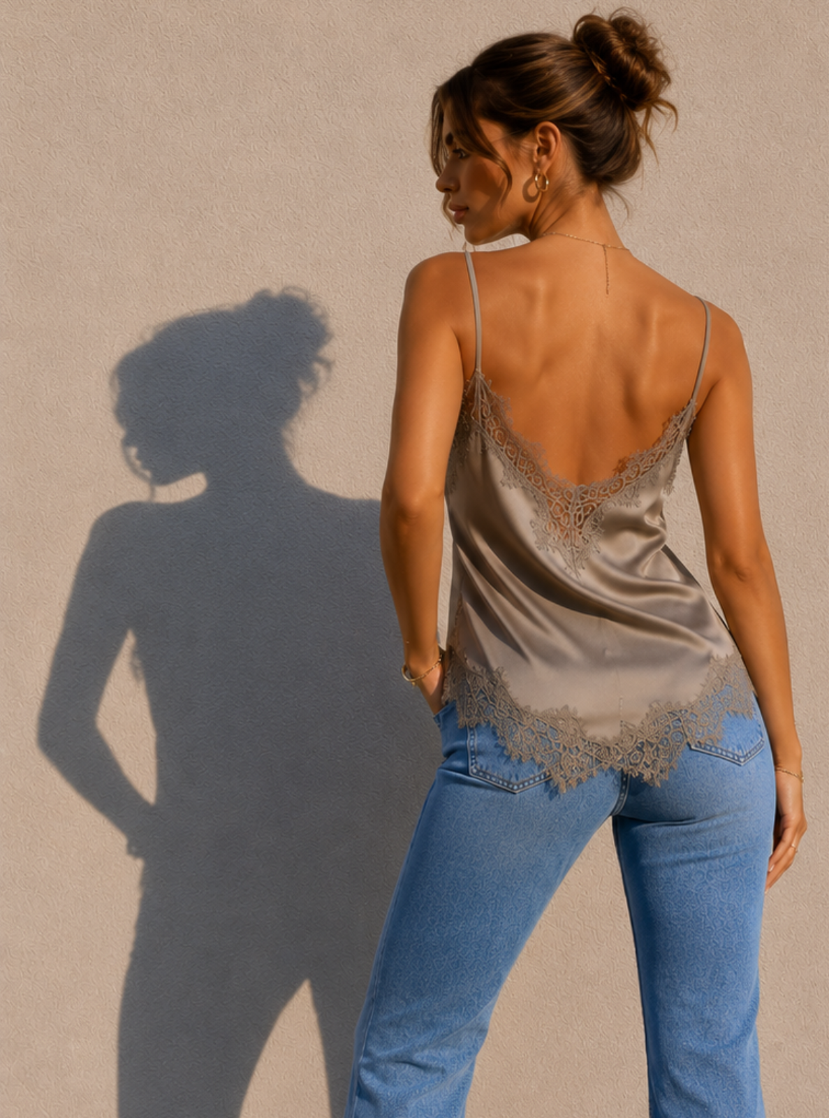 Woman wearing a lace top and blue flared jeans against a beige wall.