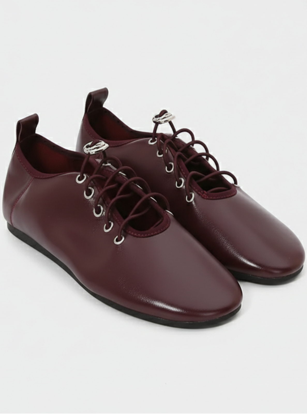 Pair of maroon shoes with silver eyelets on a white background