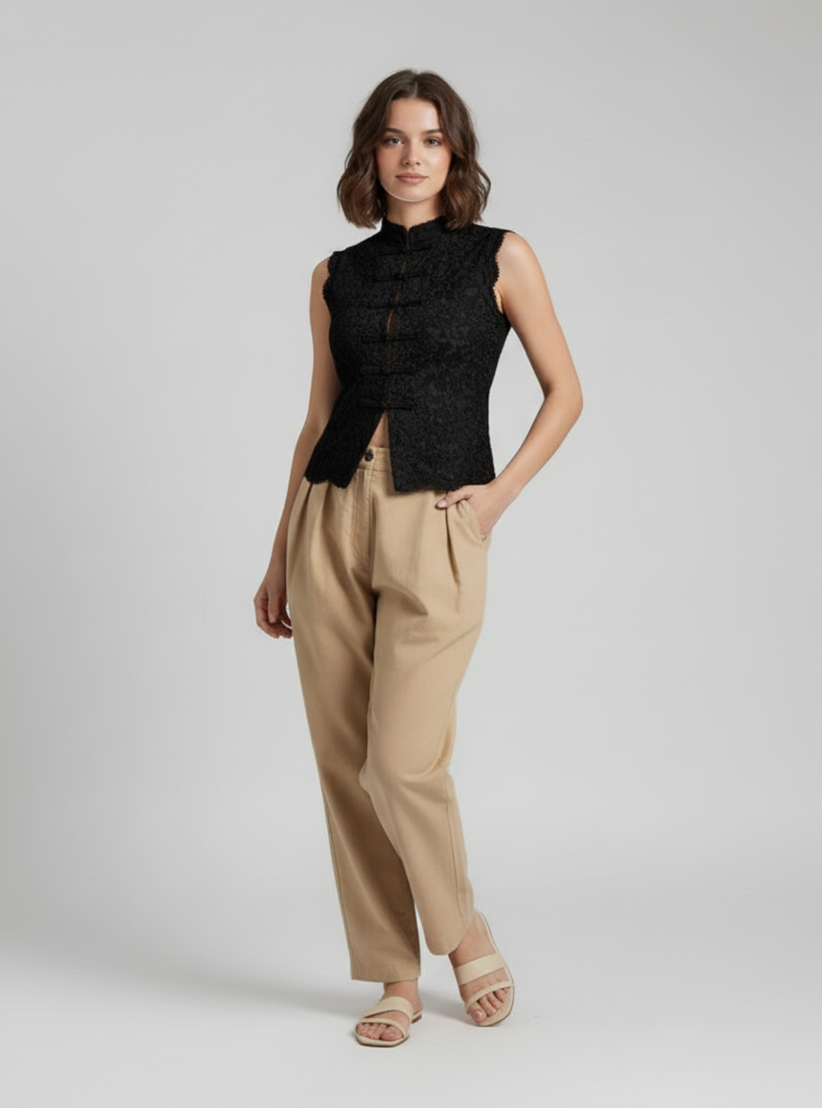 Woman wearing a black sleeveless top and beige pants on a white background