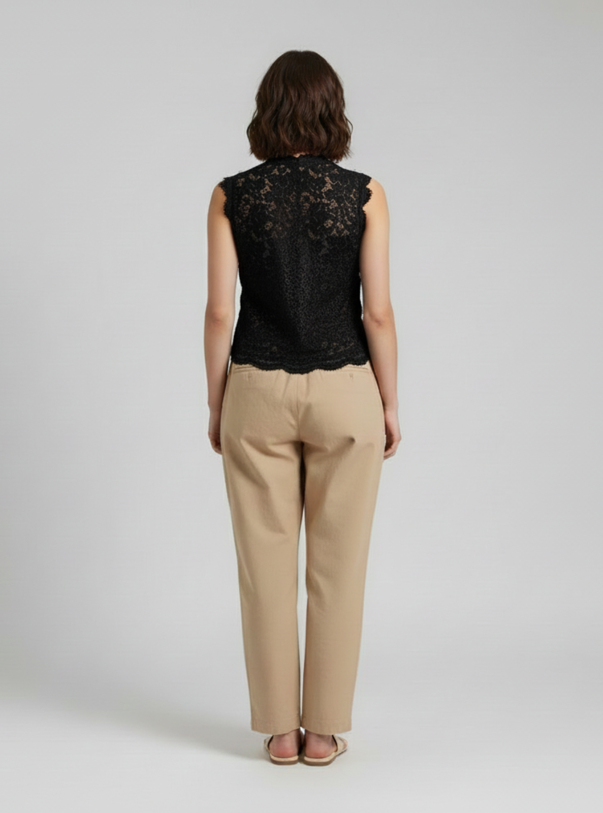 Woman wearing a black lace top and beige pants on a white background