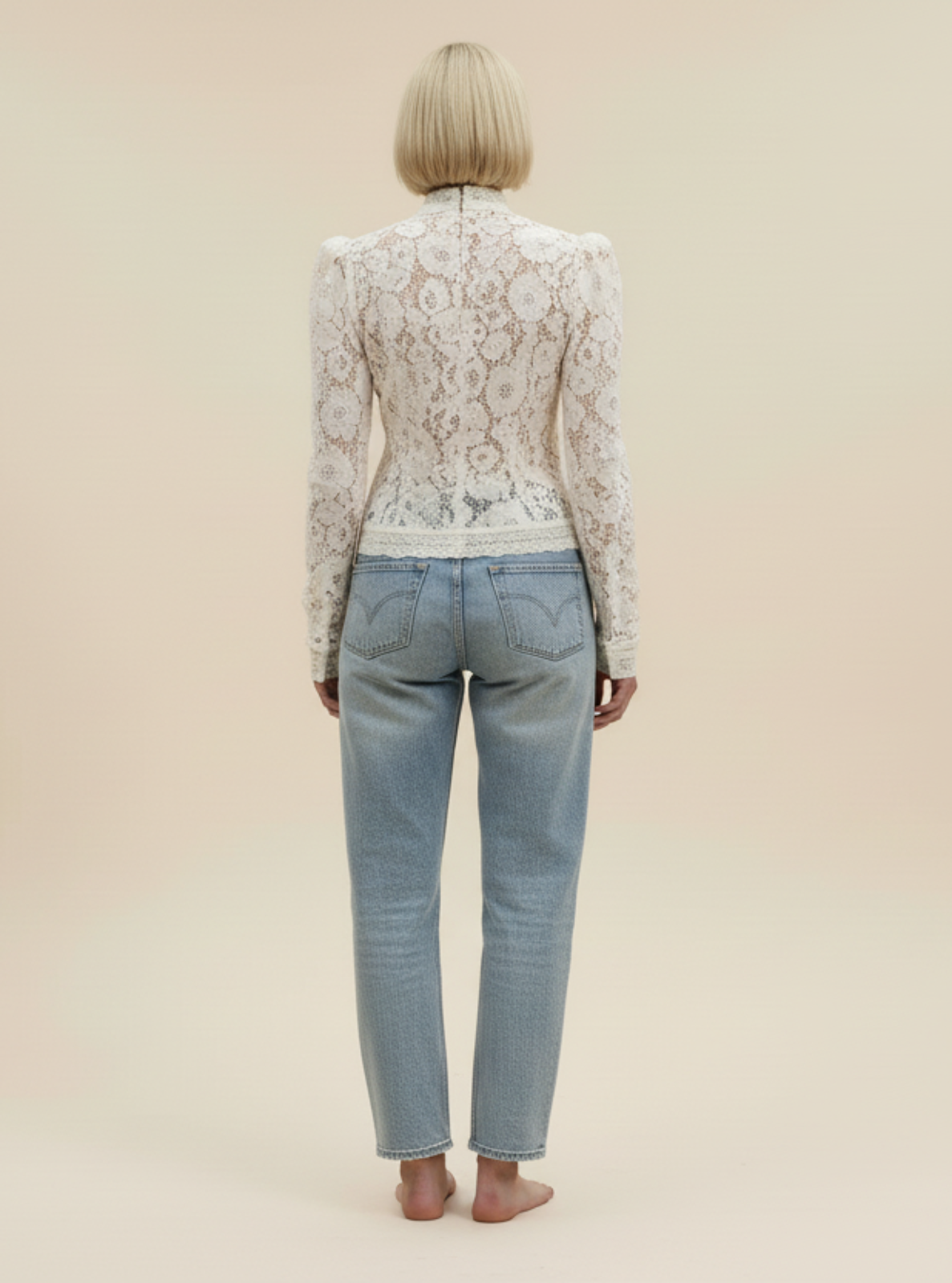 Person wearing a lace top and light blue jeans against a beige background