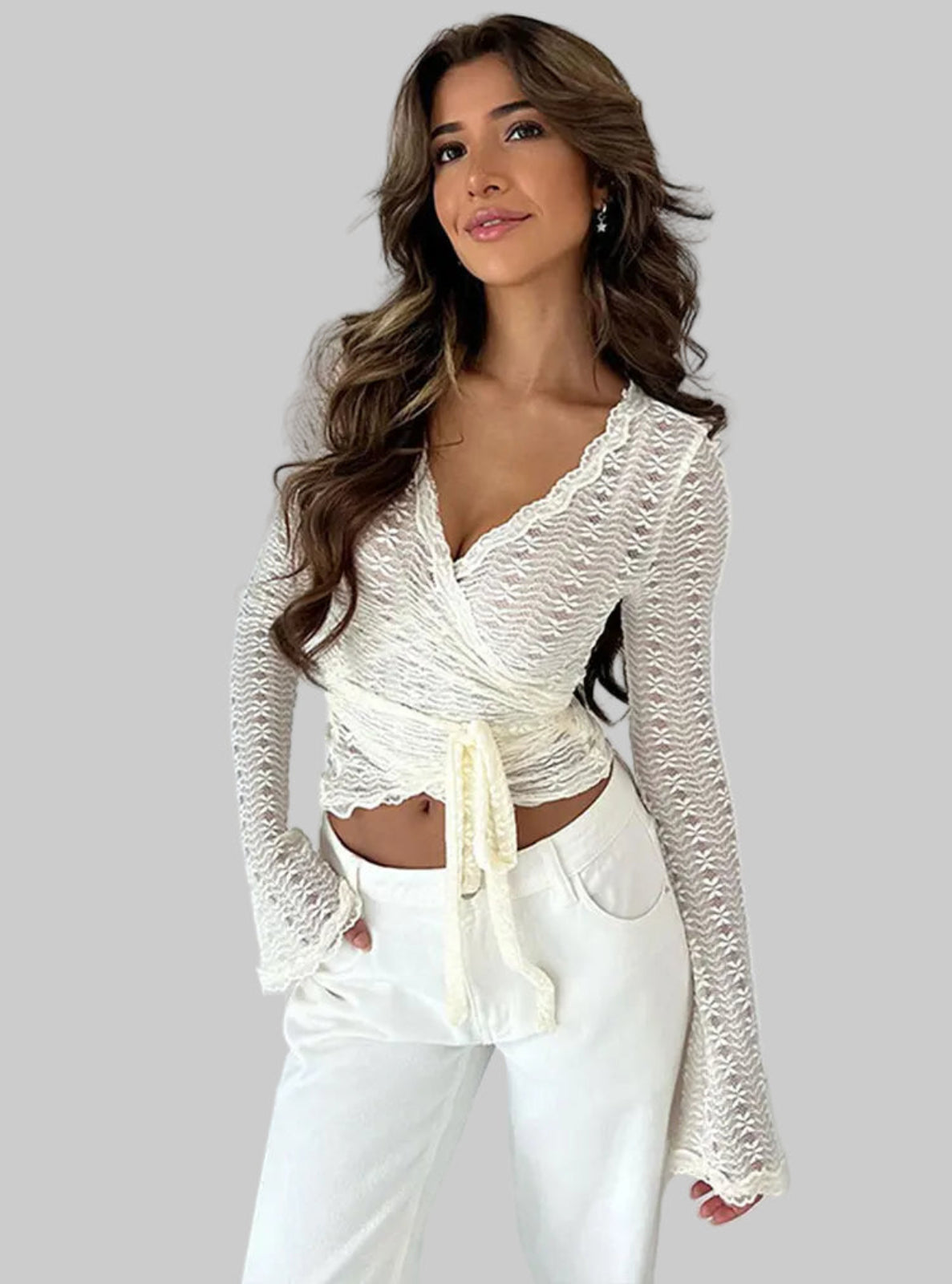 Woman wearing a white lace top and pants against a plain background