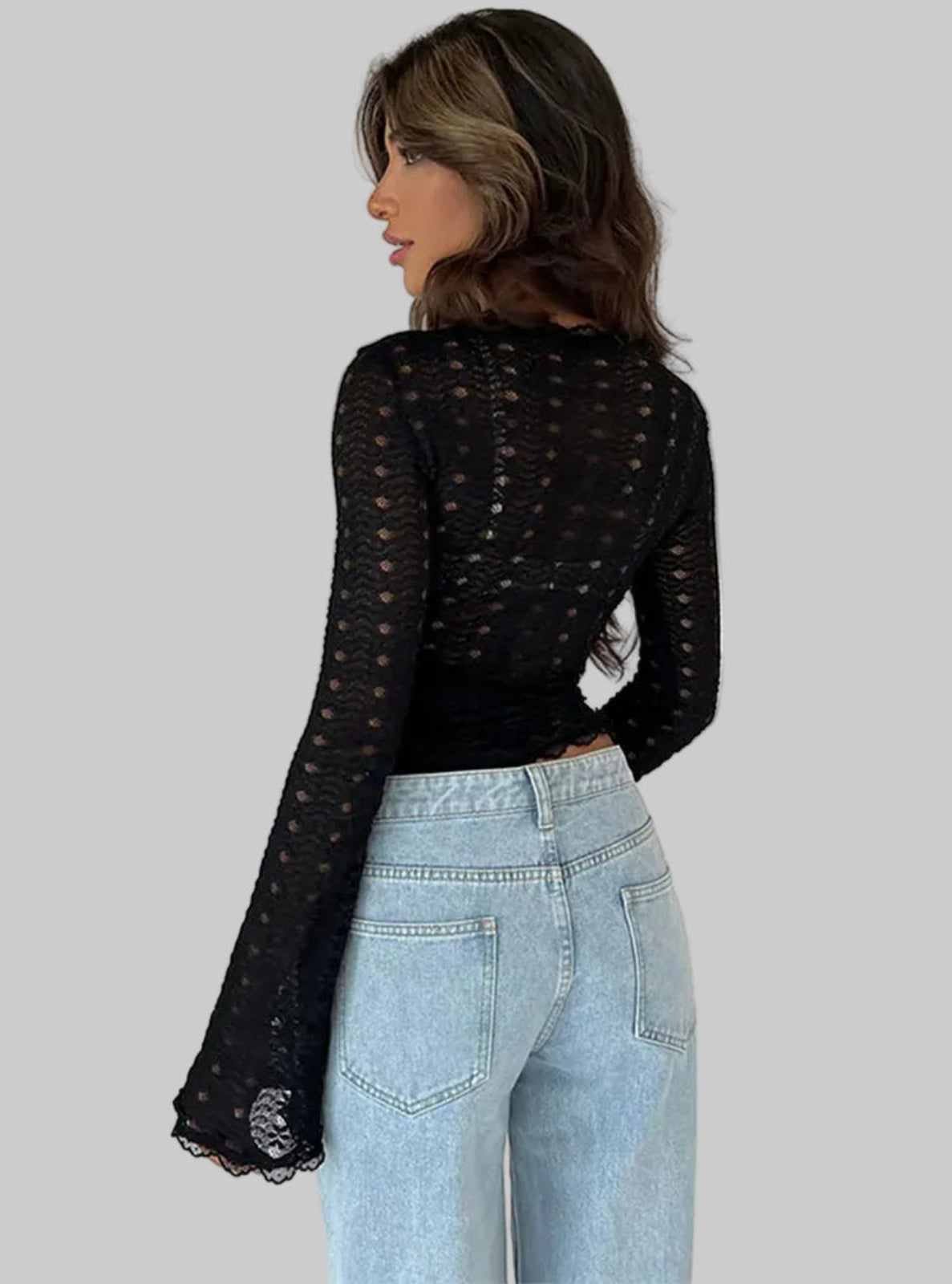 Woman wearing a black sheer long-sleeve top and light blue jeans against a white background