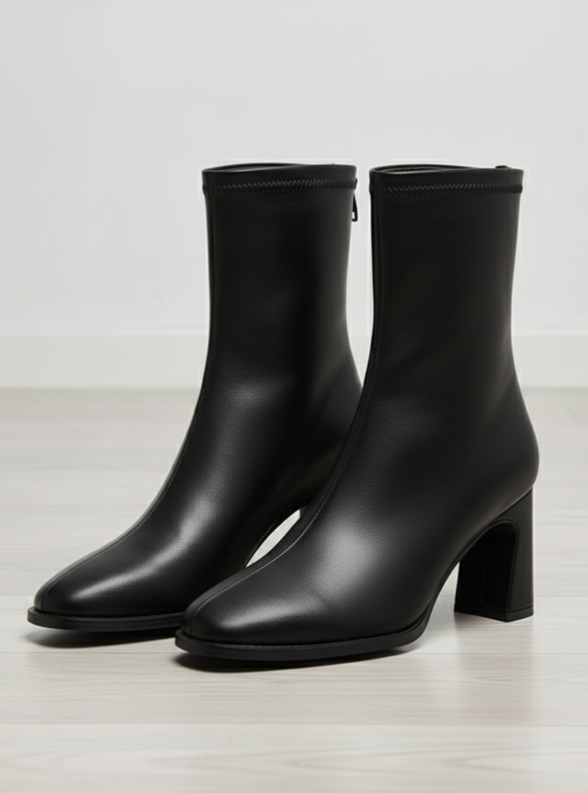 Pair of black ankle boots on a light wooden floor.