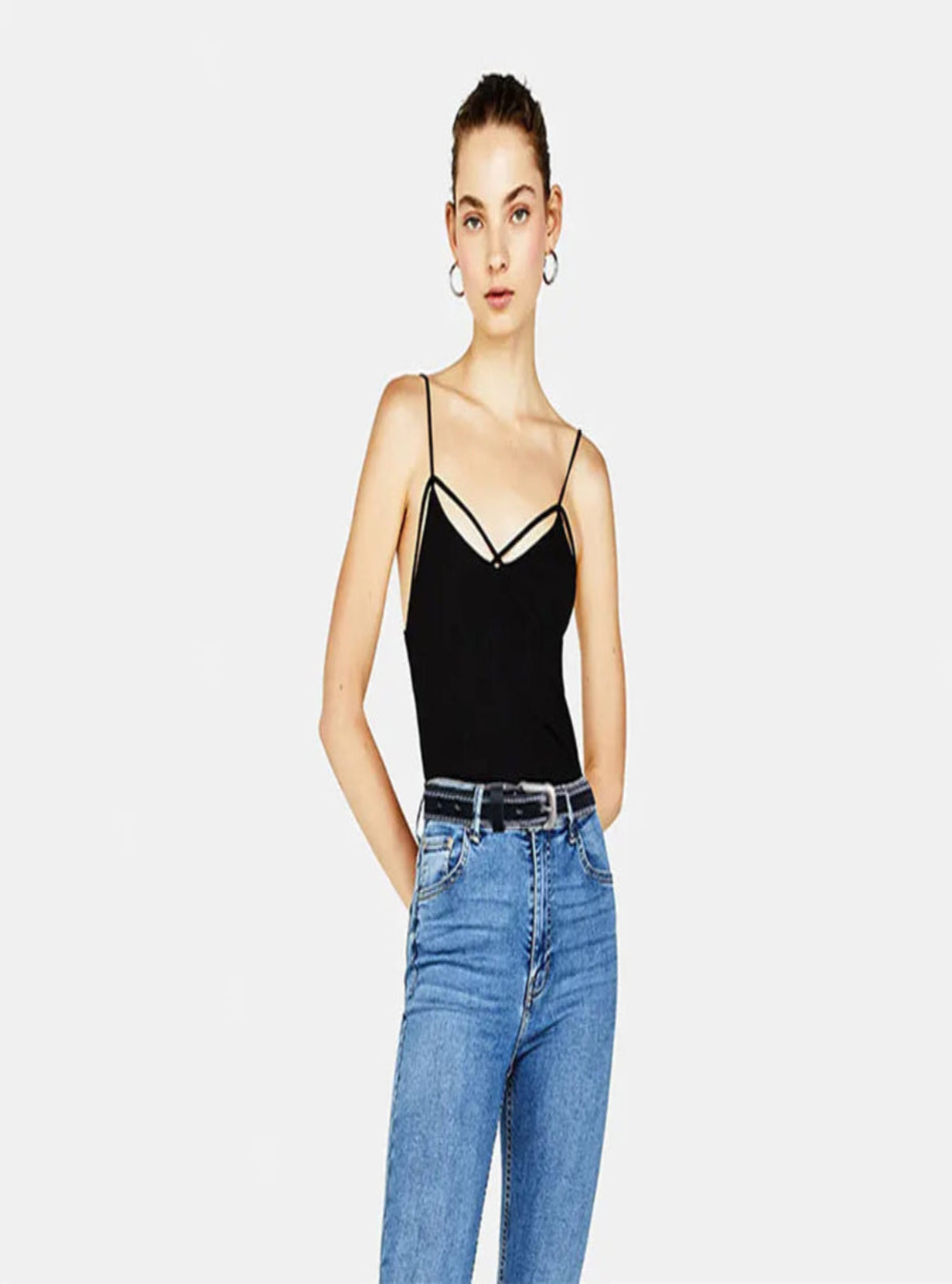Woman wearing a black strappy top and blue jeans with black leather belt on a white background