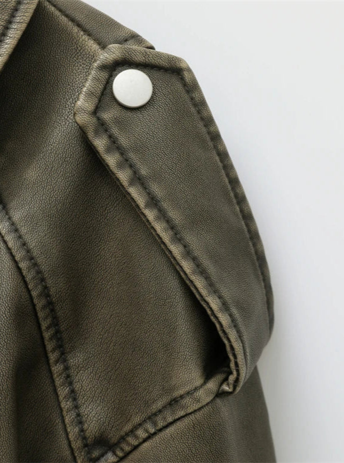 Close-up of a green leather jacket with a button on a white background