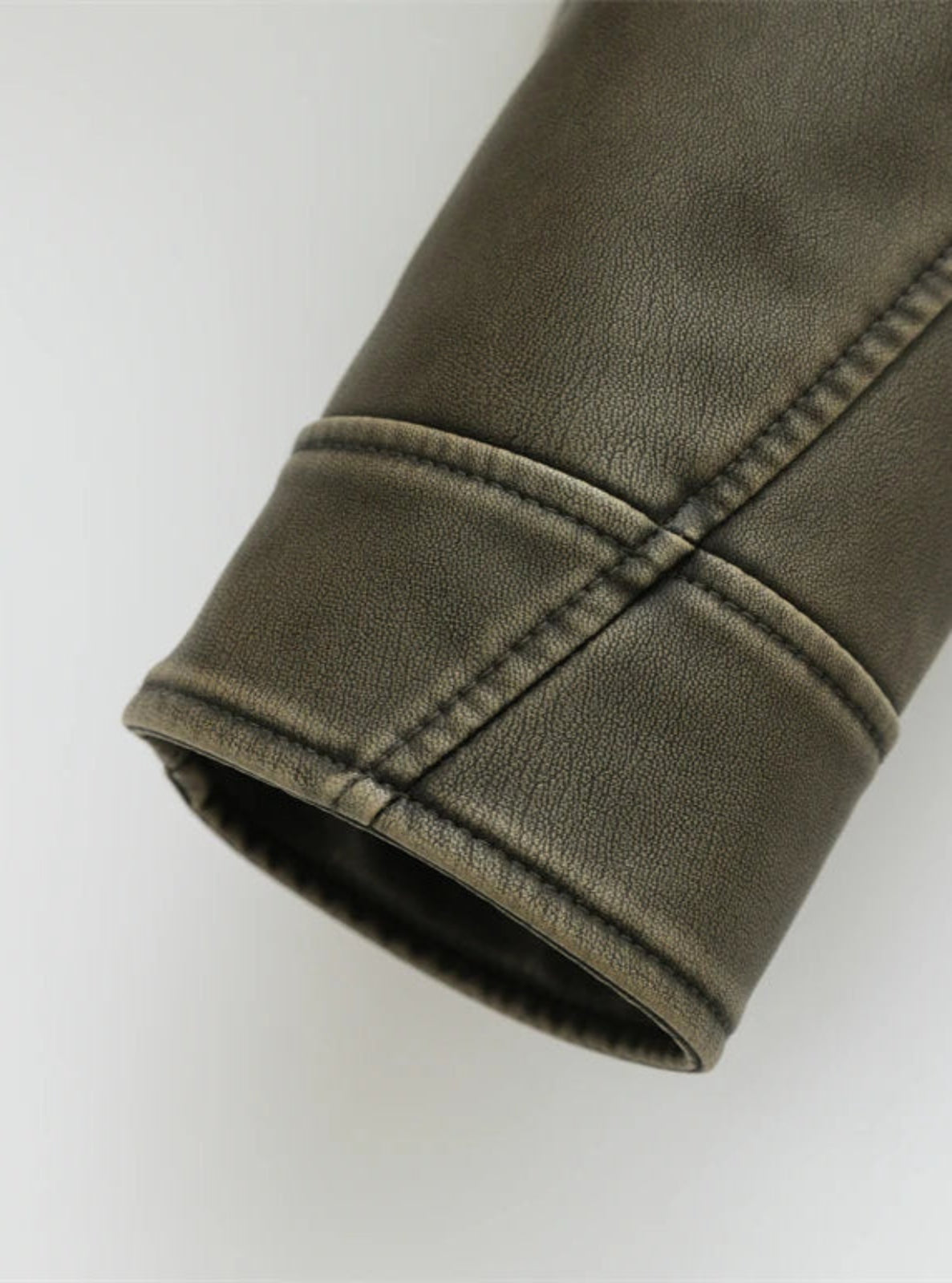 Close-up of a rolled-up sleeve of a green leather jacket on a white background
