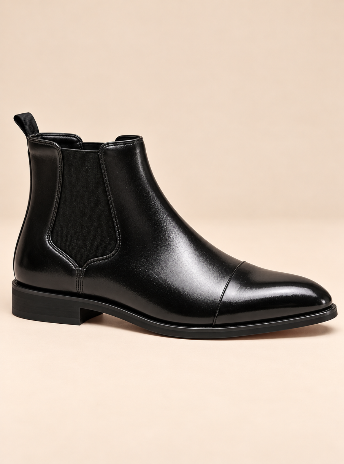 A black leather ankle boot with a cap toe and elastic side gore, shown from a side profile on a solid beige background.