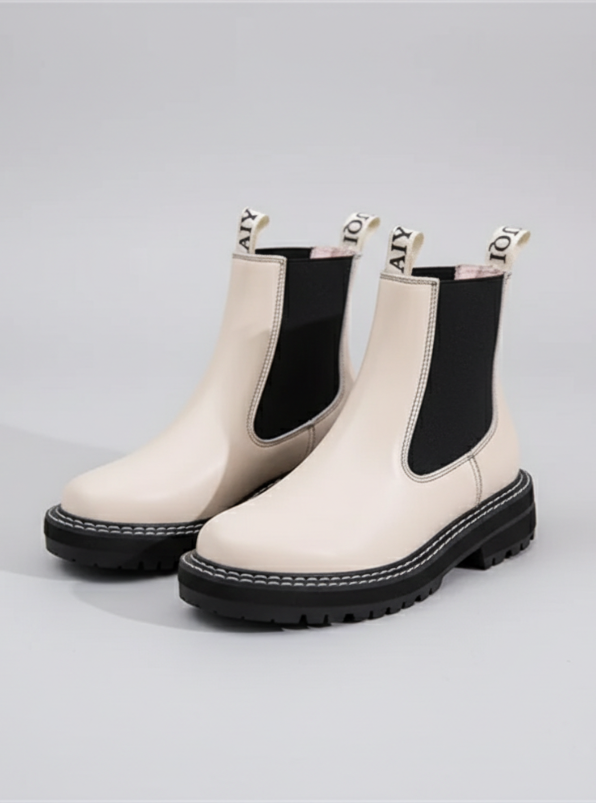 Pair of beige Chelsea boots with black soles on a light gray background