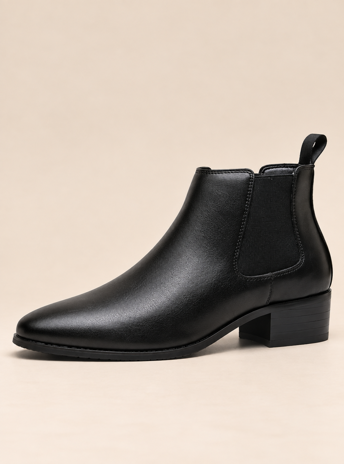 A single black leather Chelsea-style ankle boot with a low block heel and elastic side gore, photographed on a plain warm beige studio background.