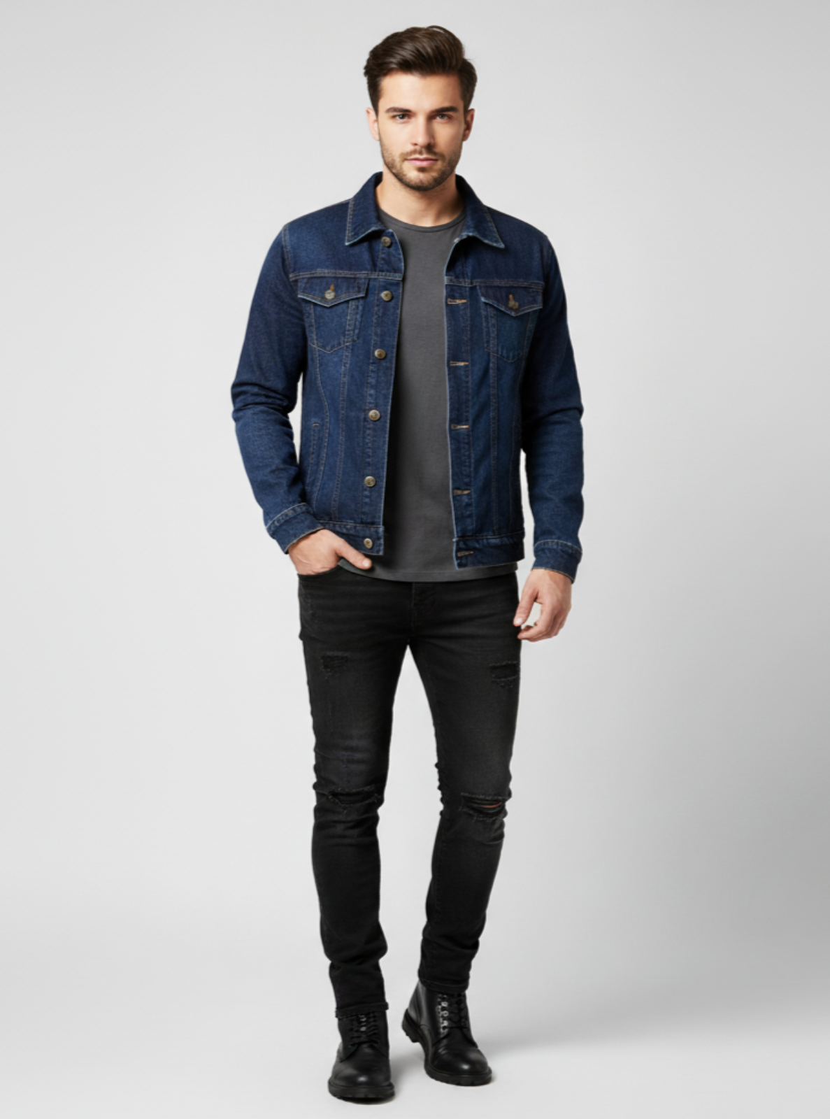Man wearing a denim jacket, gray shirt, black pants, and black boots on a light gray background