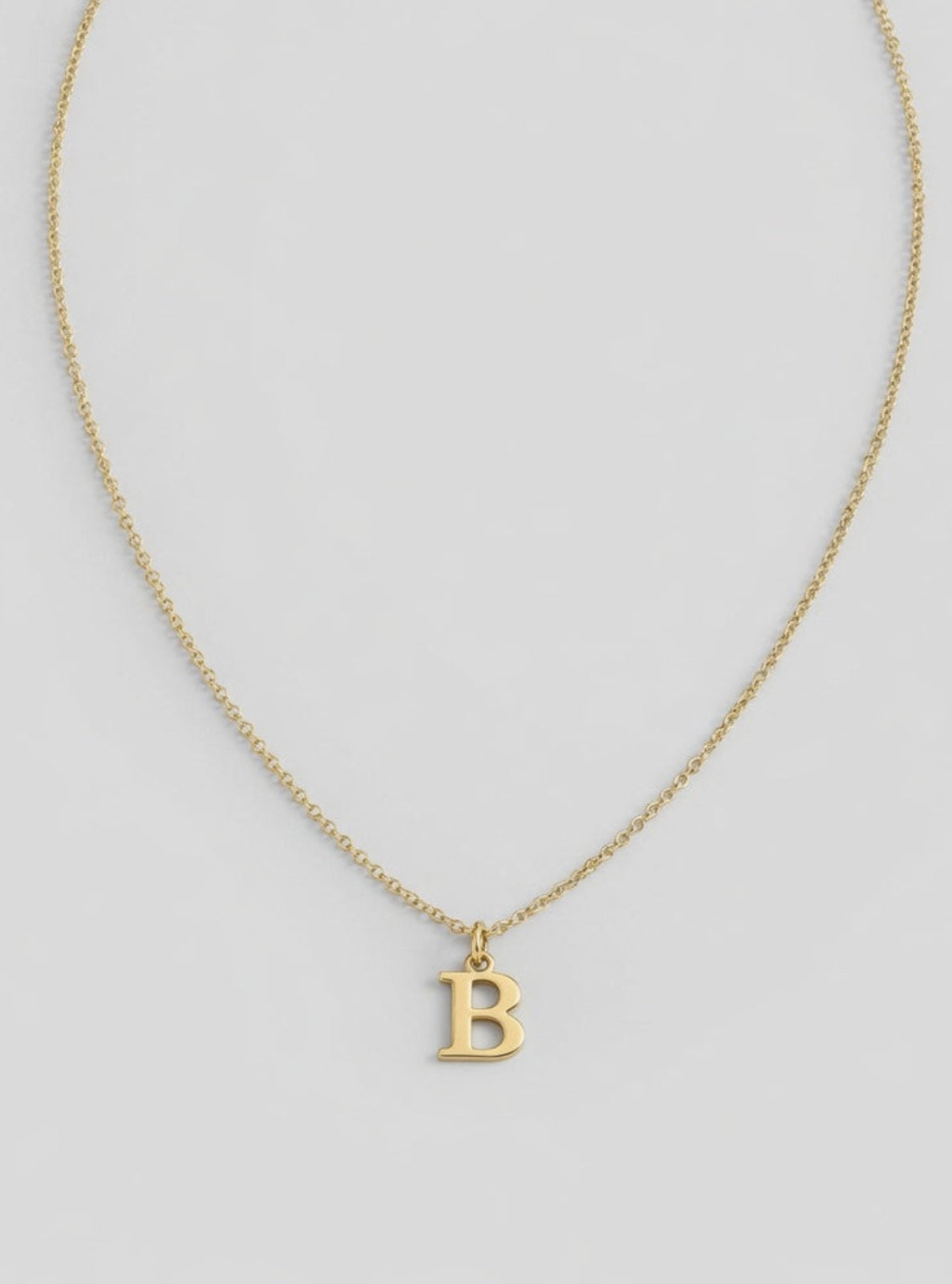 Gold necklace with a 'B' pendant on a light gray background