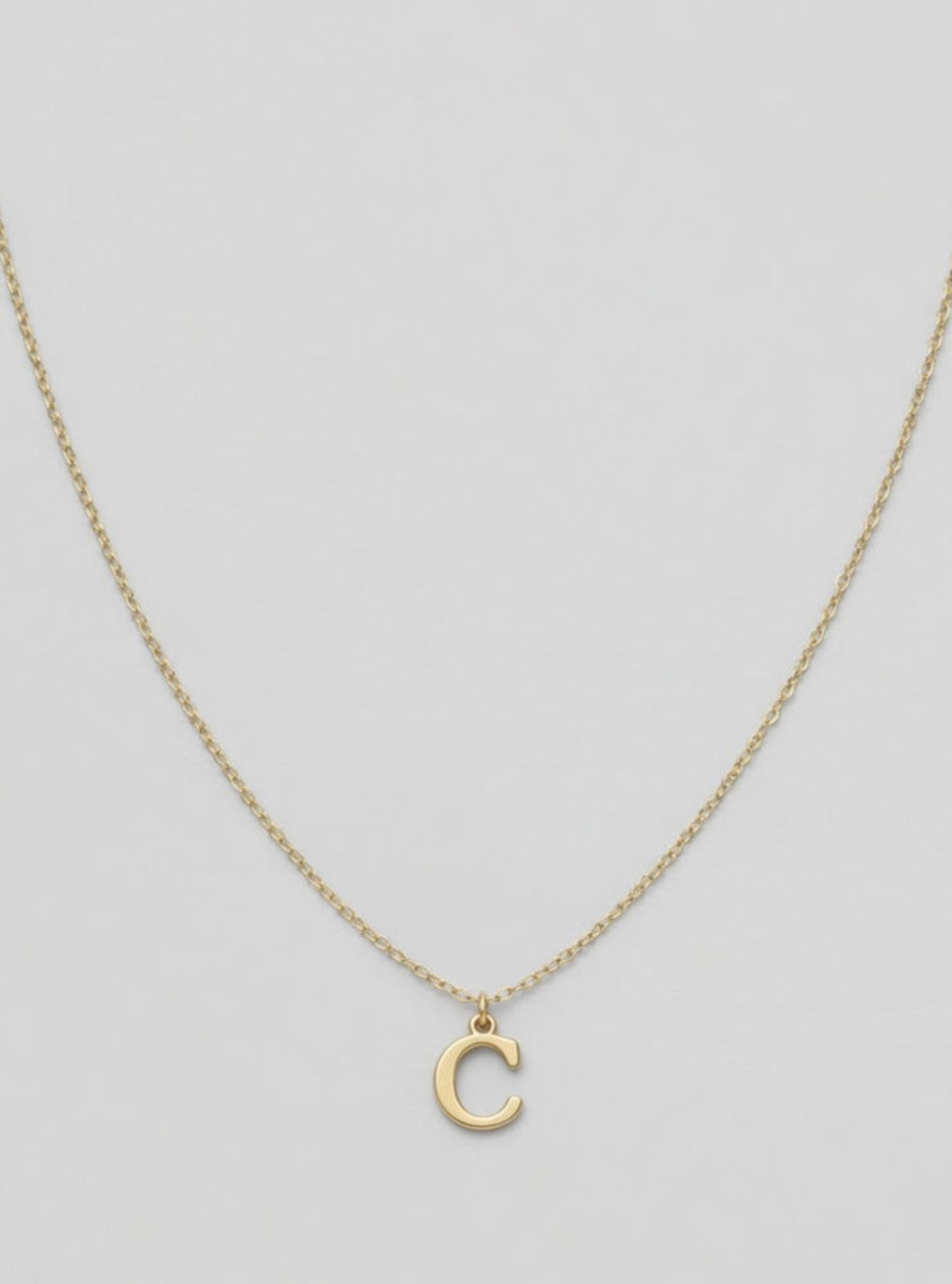 Gold necklace with a 'C' pendant on a light gray background