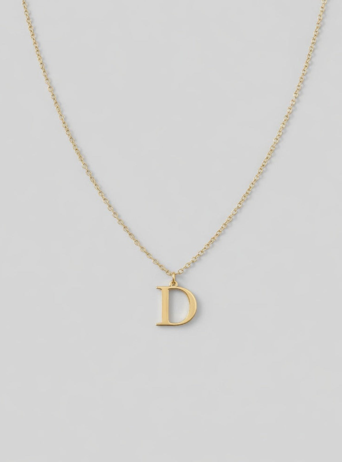 Gold necklace with a 'D' pendant on a light gray background