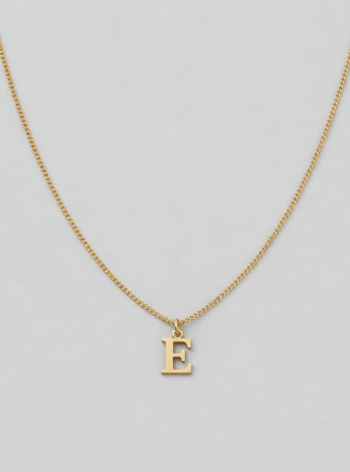 Gold necklace with a 'E' pendant on a light gray background