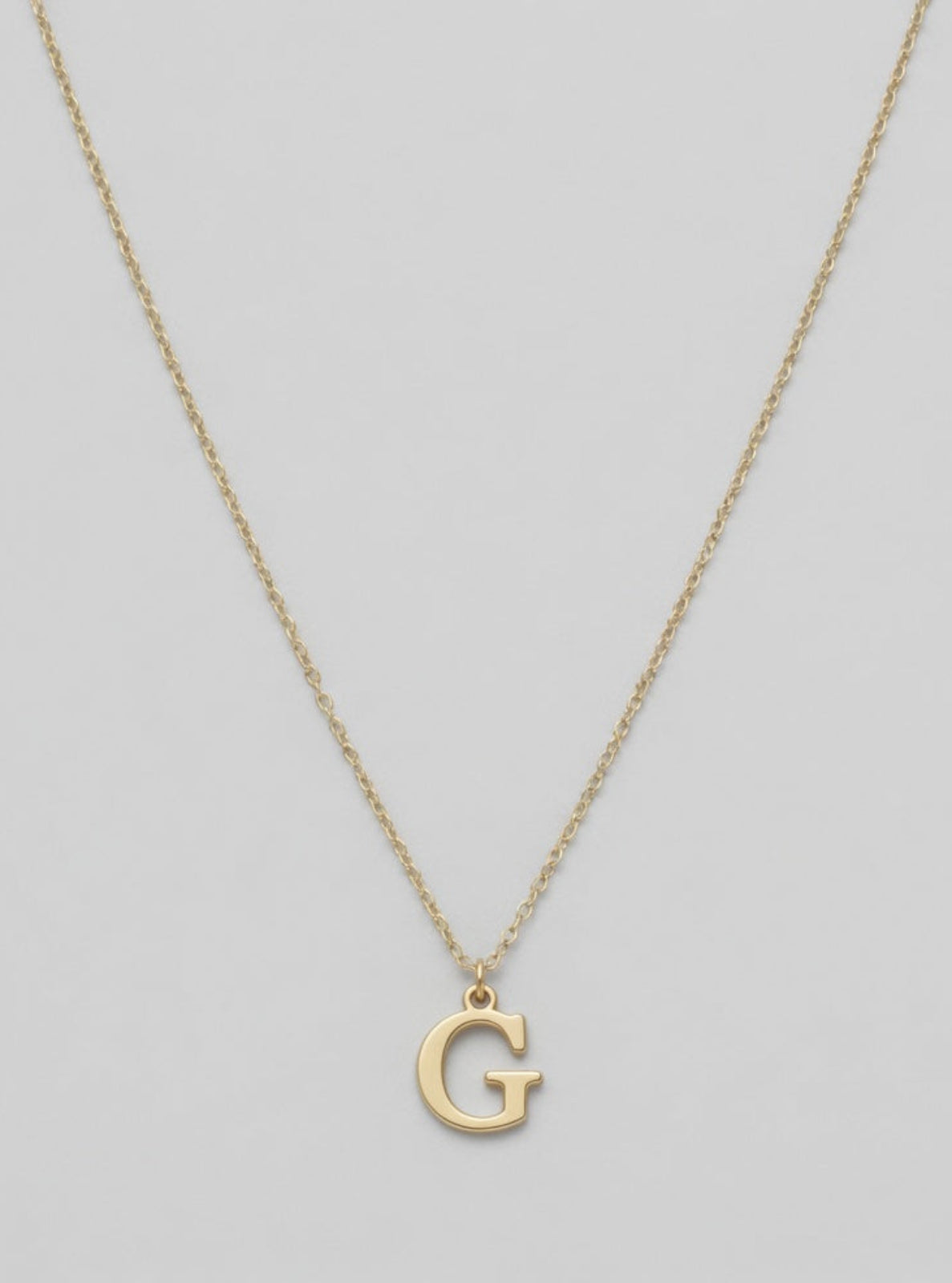 Gold necklace with a 'G' pendant on a light gray background