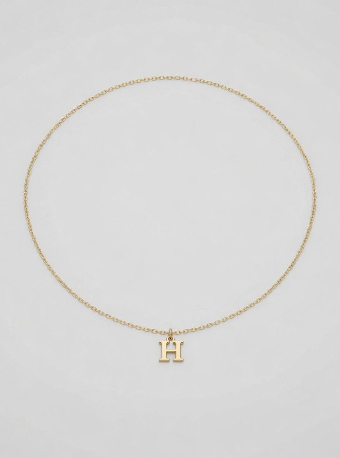 Gold necklace with a 'H' pendant on a light gray background