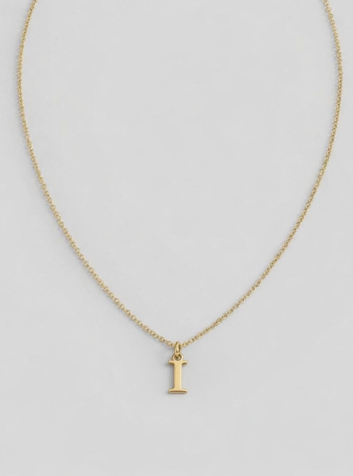 Gold necklace with a letter 'I' pendant on a light gray background