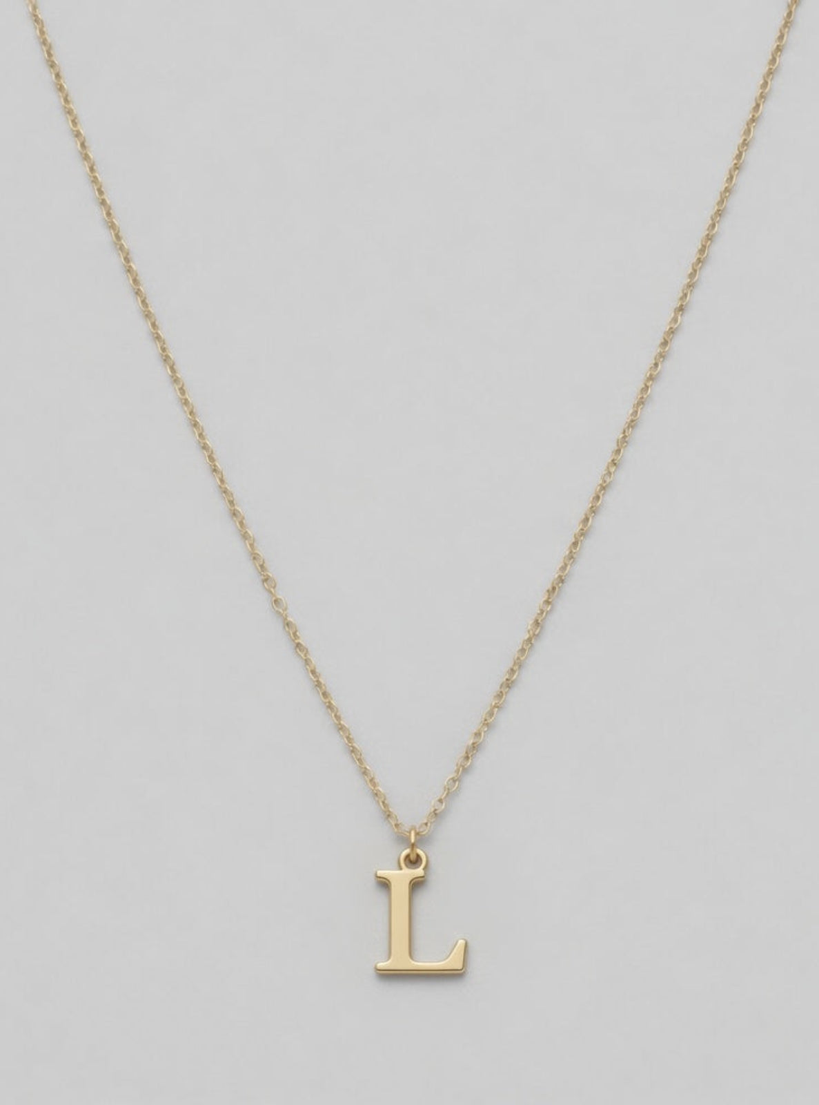 Gold necklace with a 'L' pendant on a light gray background