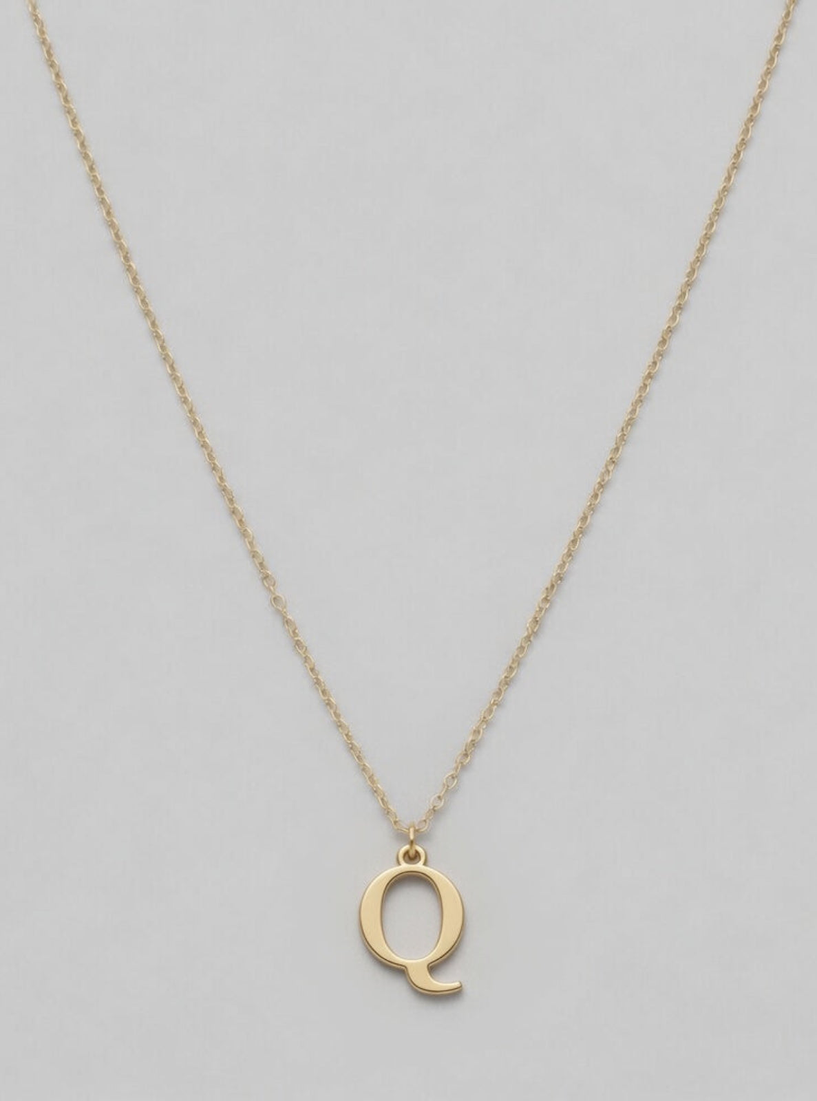 Gold necklace with a 'Q' pendant on a light gray background