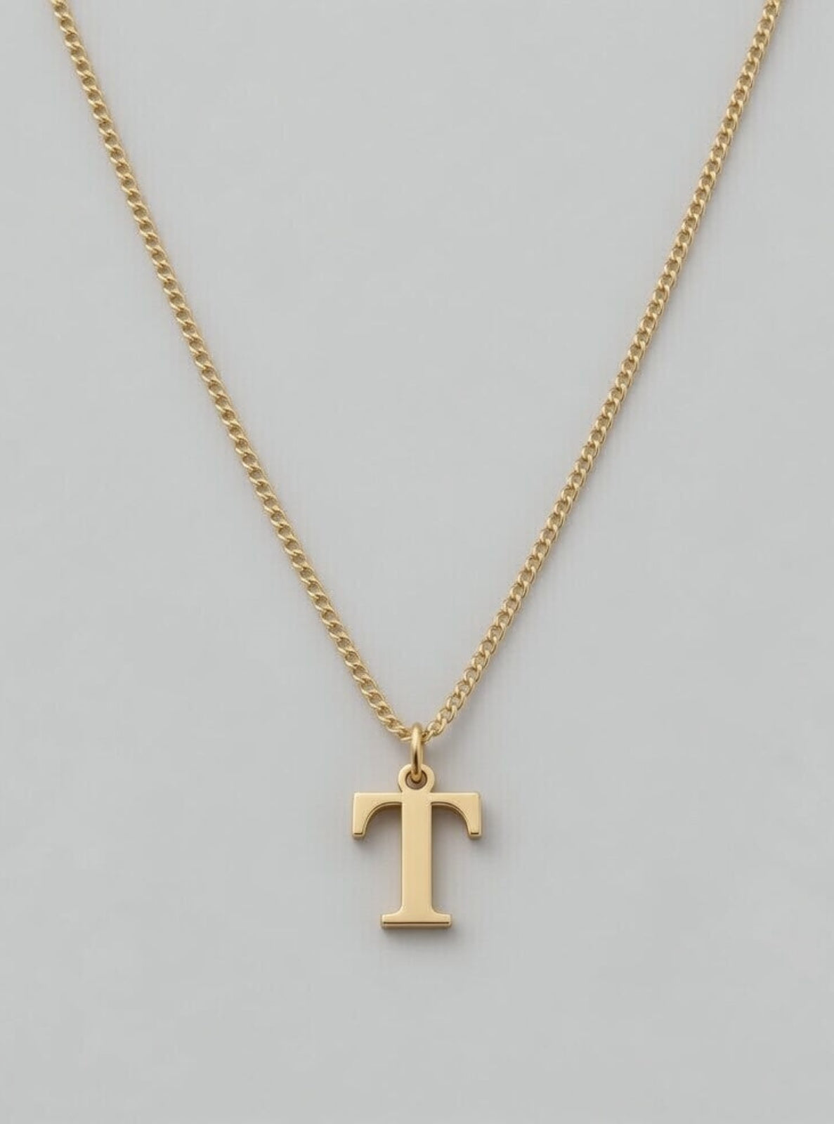 Gold necklace with a 'T' pendant on a gray background