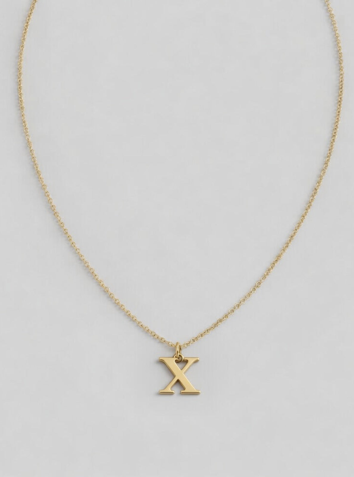 Gold necklace with a 'X' pendant on a light gray background
