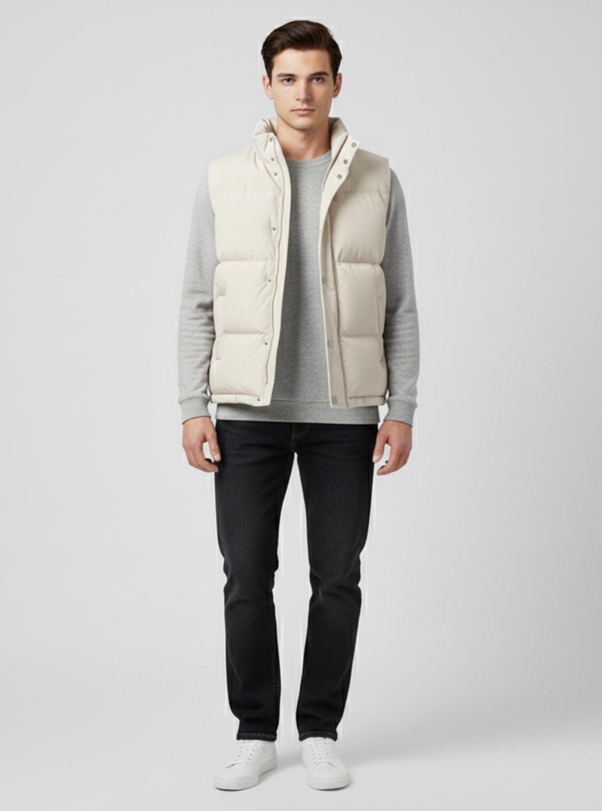 Man wearing a light gray vest over a gray sweater with black pants on a white background