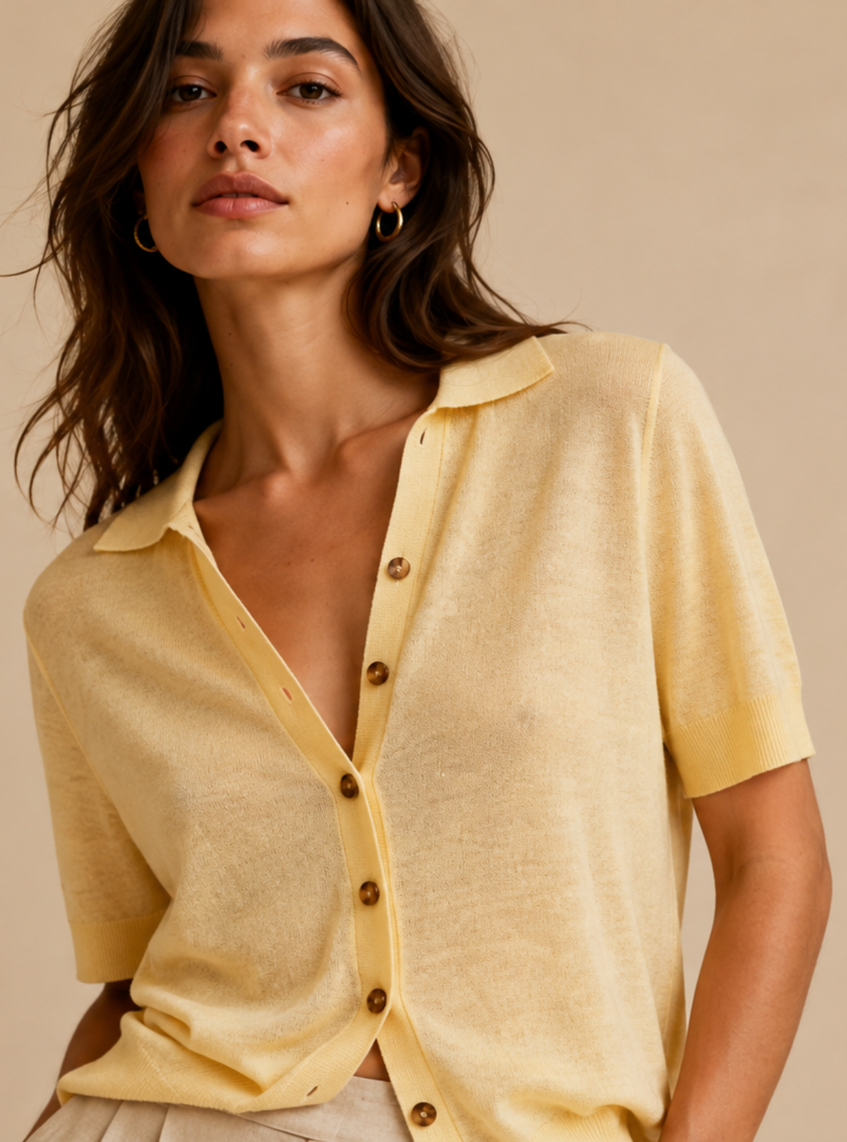A woman wearing a pale yellow short-sleeve button-front knit top with a collar, photographed against a plain warm beige studio background.