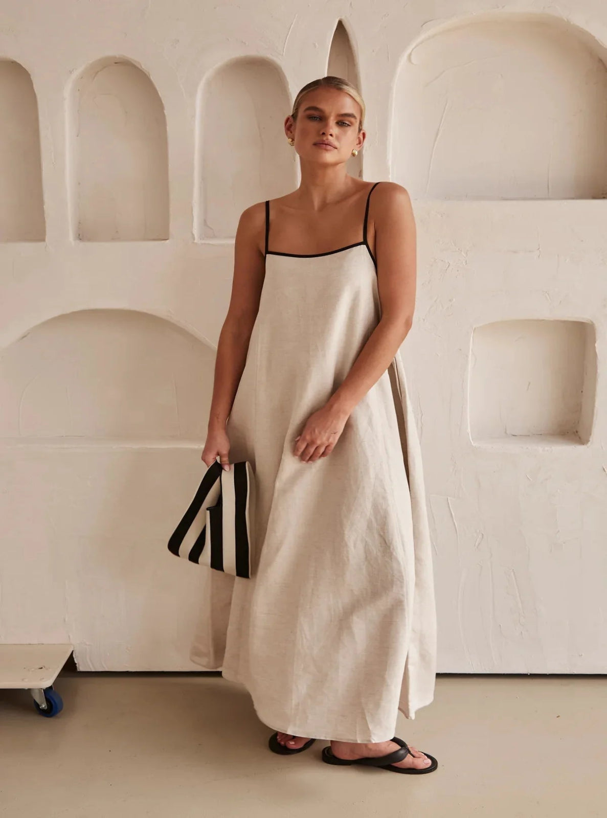 Woman in a long white dress standing against a neutral wall.