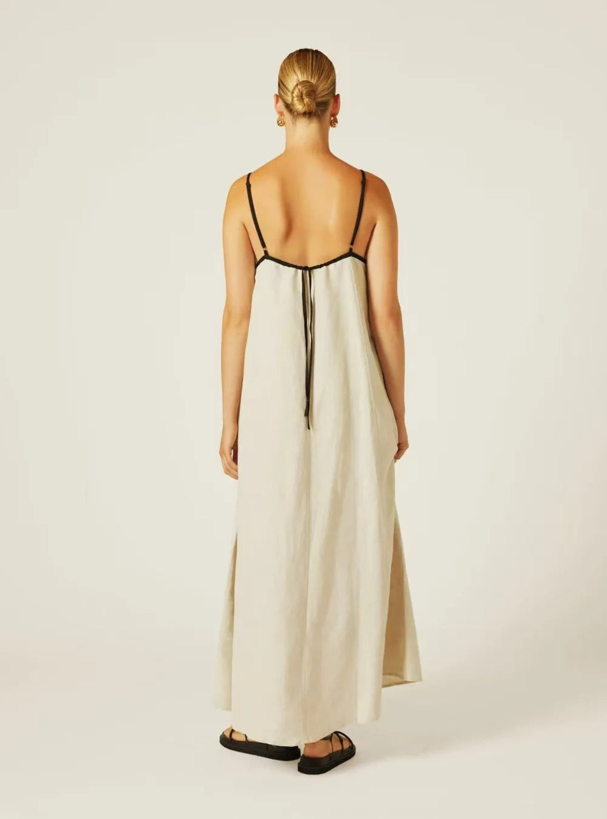 Woman wearing a long, light-colored dress with thin straps on a white background