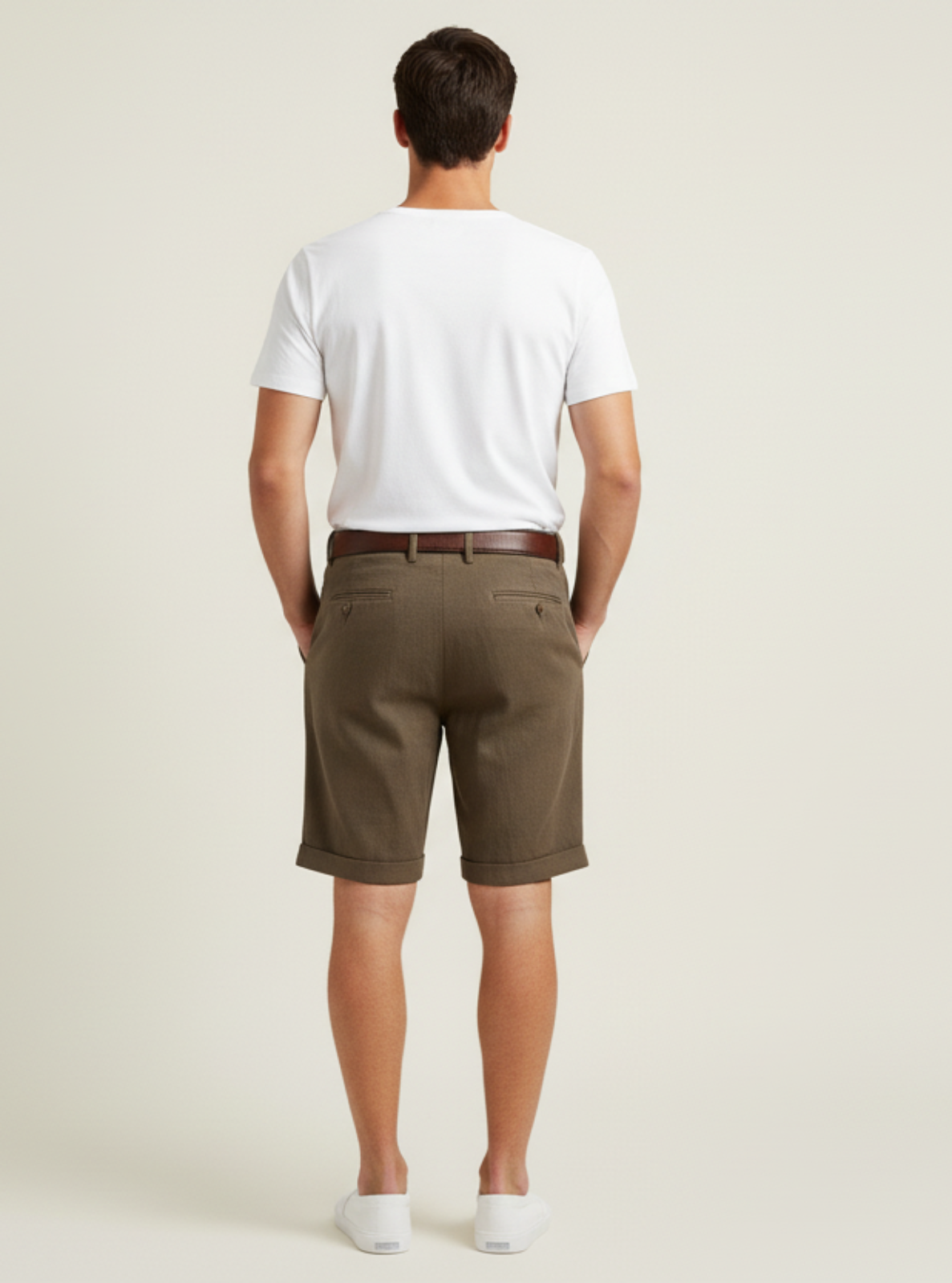 Man wearing a white t-shirt and brown shorts on a plain background