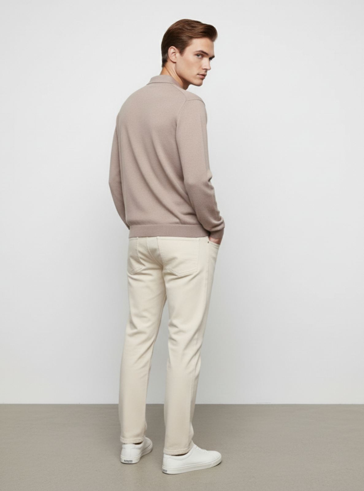 Man wearing a beige sweater and light-colored pants against a white background