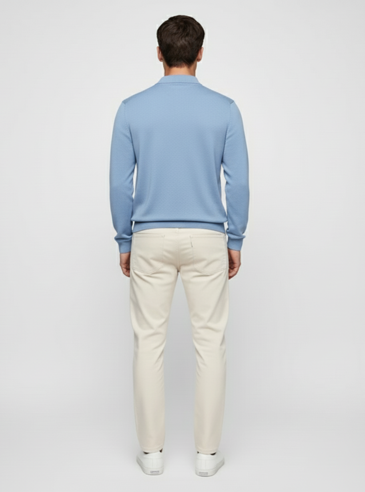 Man wearing a light blue sweater and white pants on a plain background