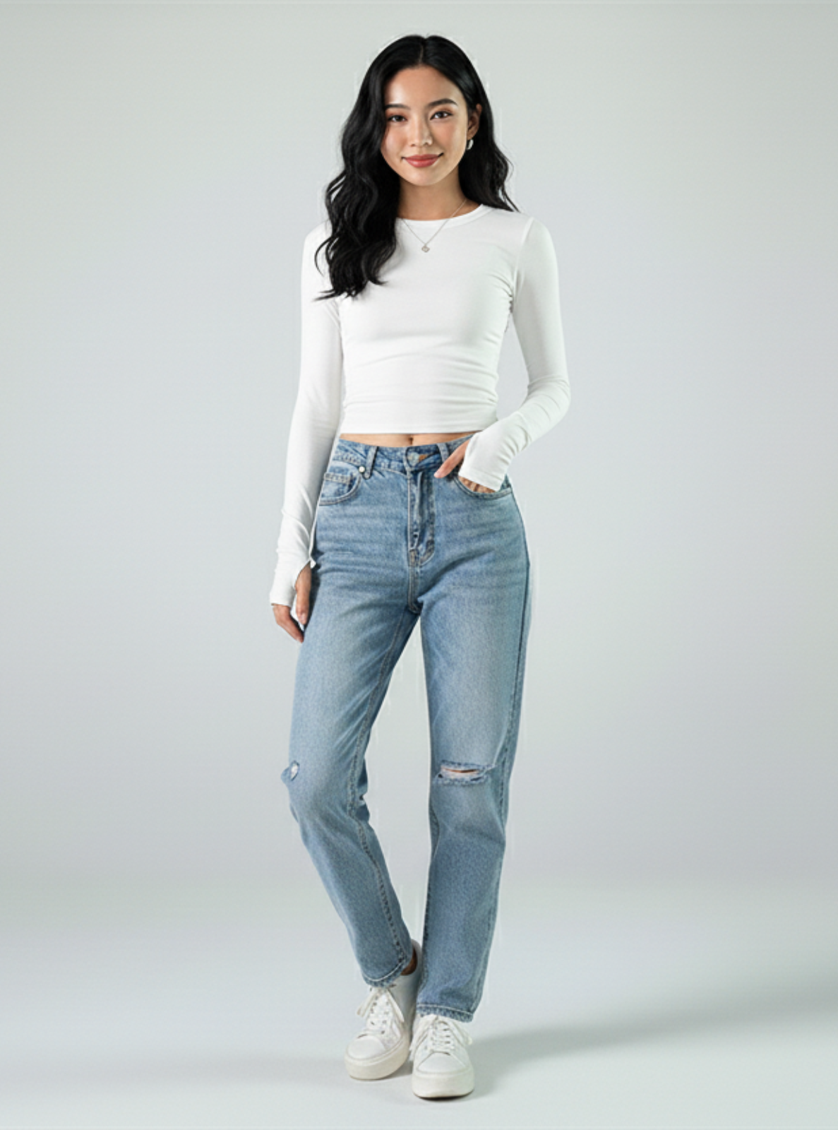 Woman wearing a white long-sleeve shirt and light blue jeans on a plain background