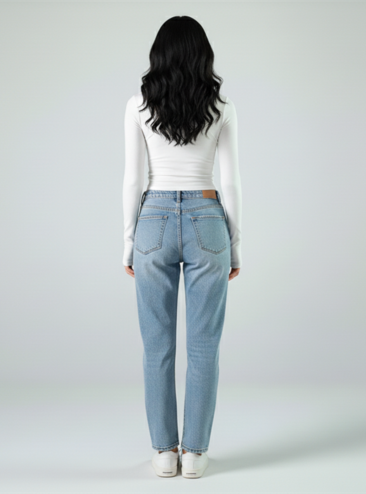 Person wearing light blue jeans and a white top on a plain background