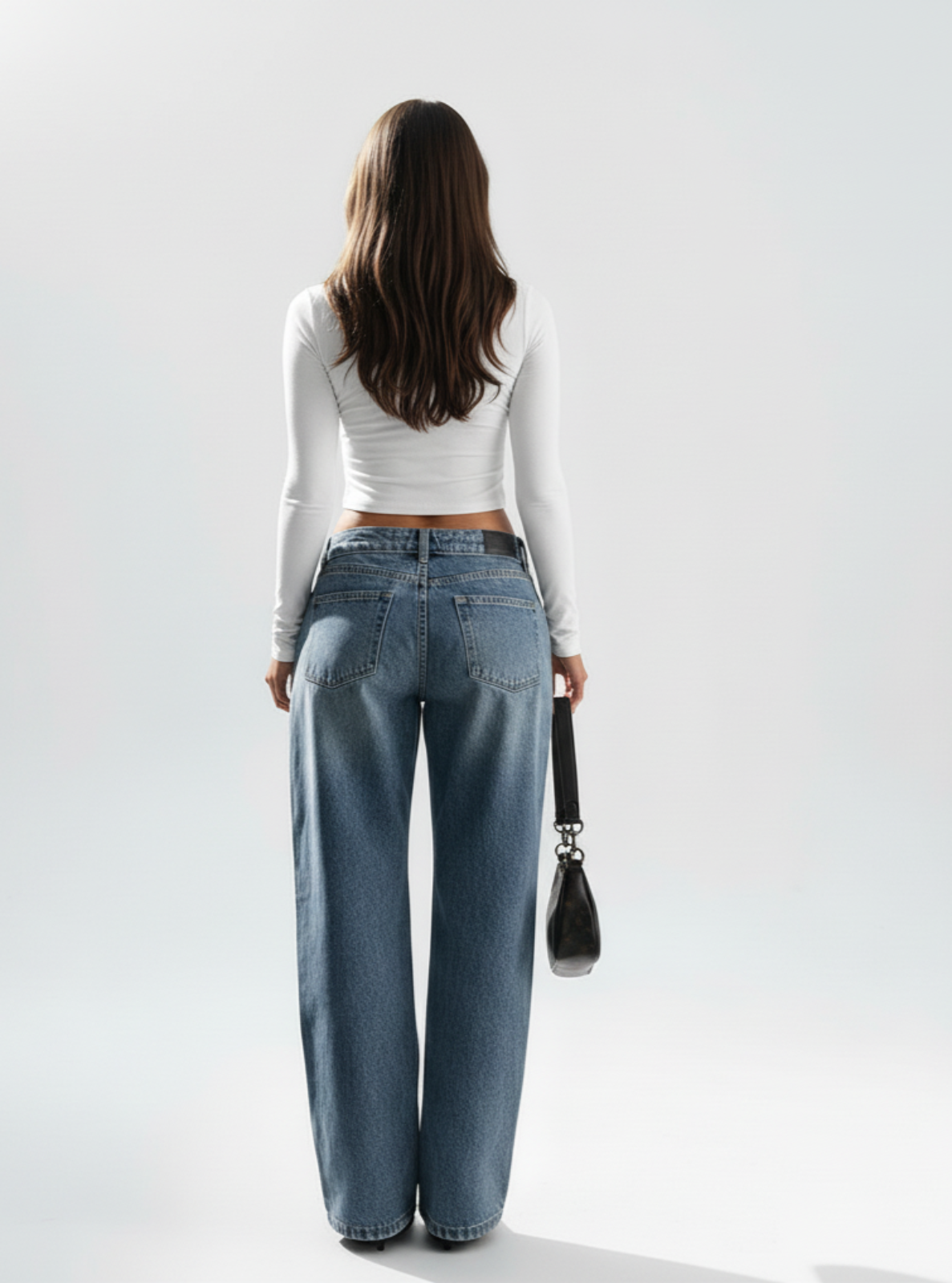 Person wearing blue jeans and a white top against a plain background