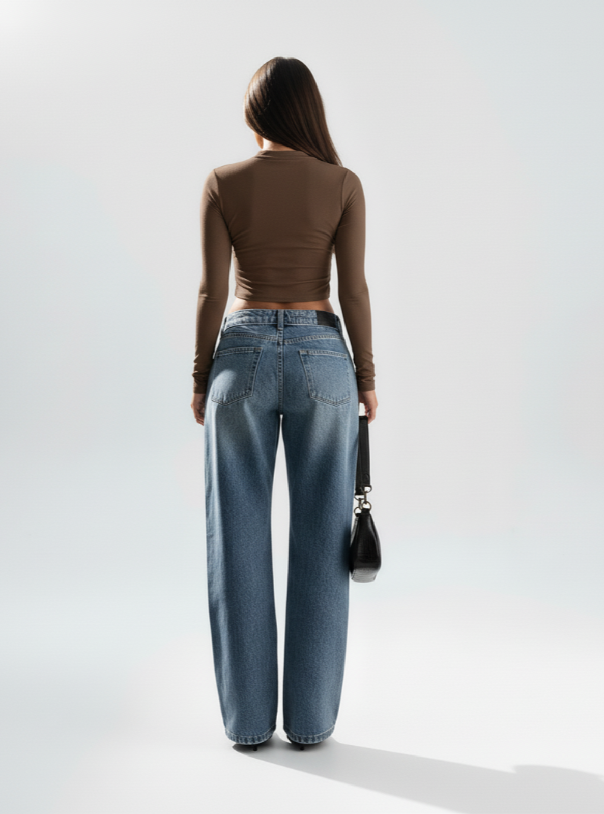 Person wearing a brown top and blue jeans against a white background