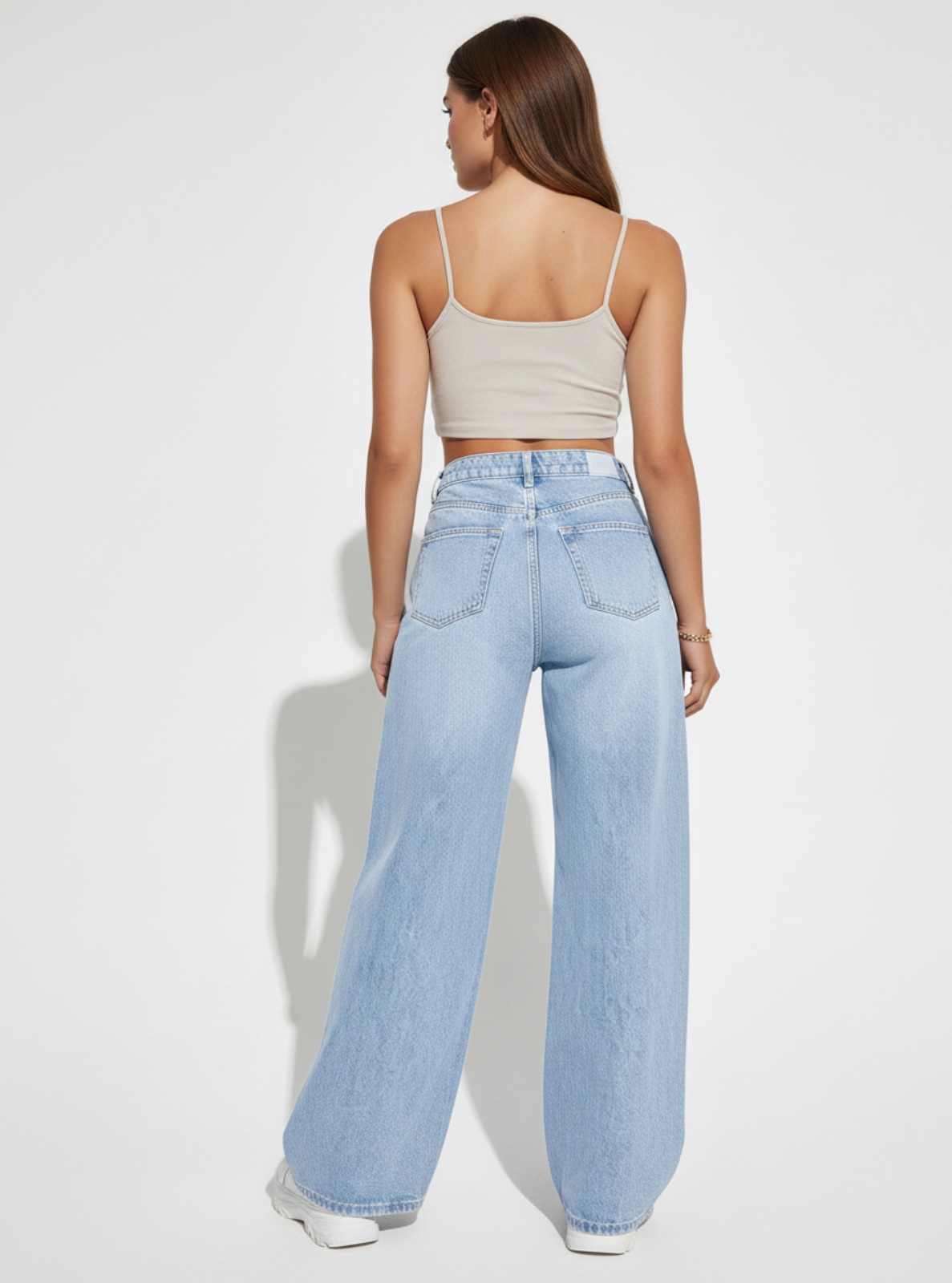 Woman wearing light blue jeans and a beige top on a white background