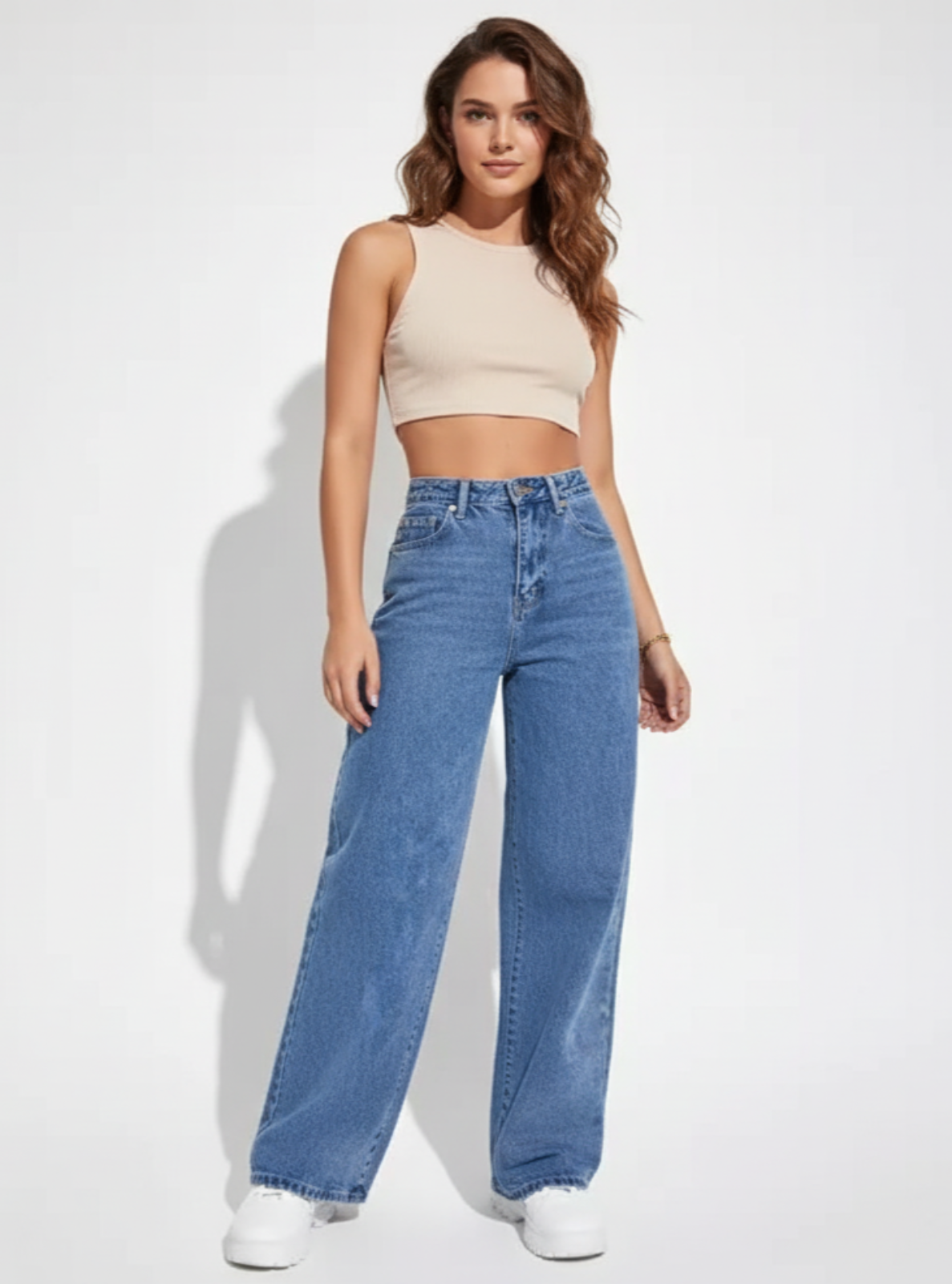 Woman wearing a beige crop top and blue jeans on a white background