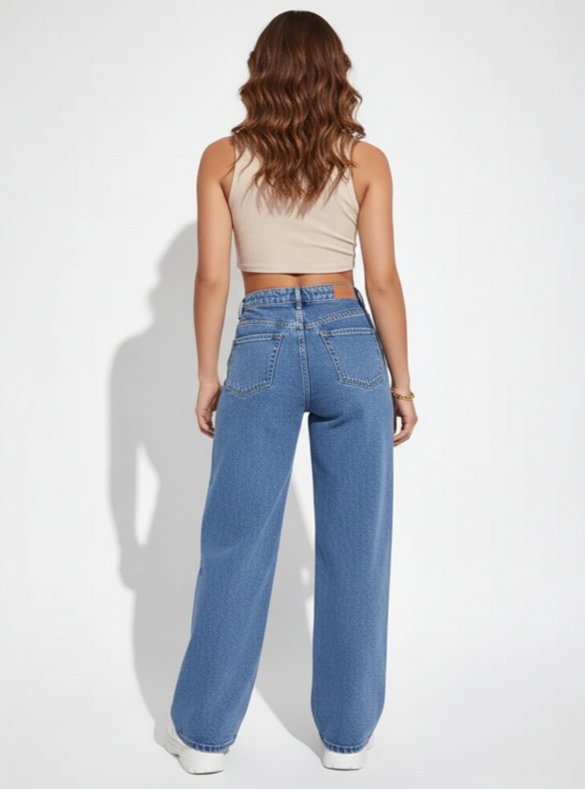 Person wearing blue jeans and a beige top on a white background