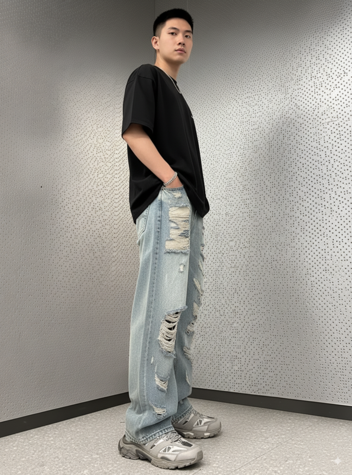 Person wearing a black oversized t-shirt and light blue ripped jeans against a gray textured wall.