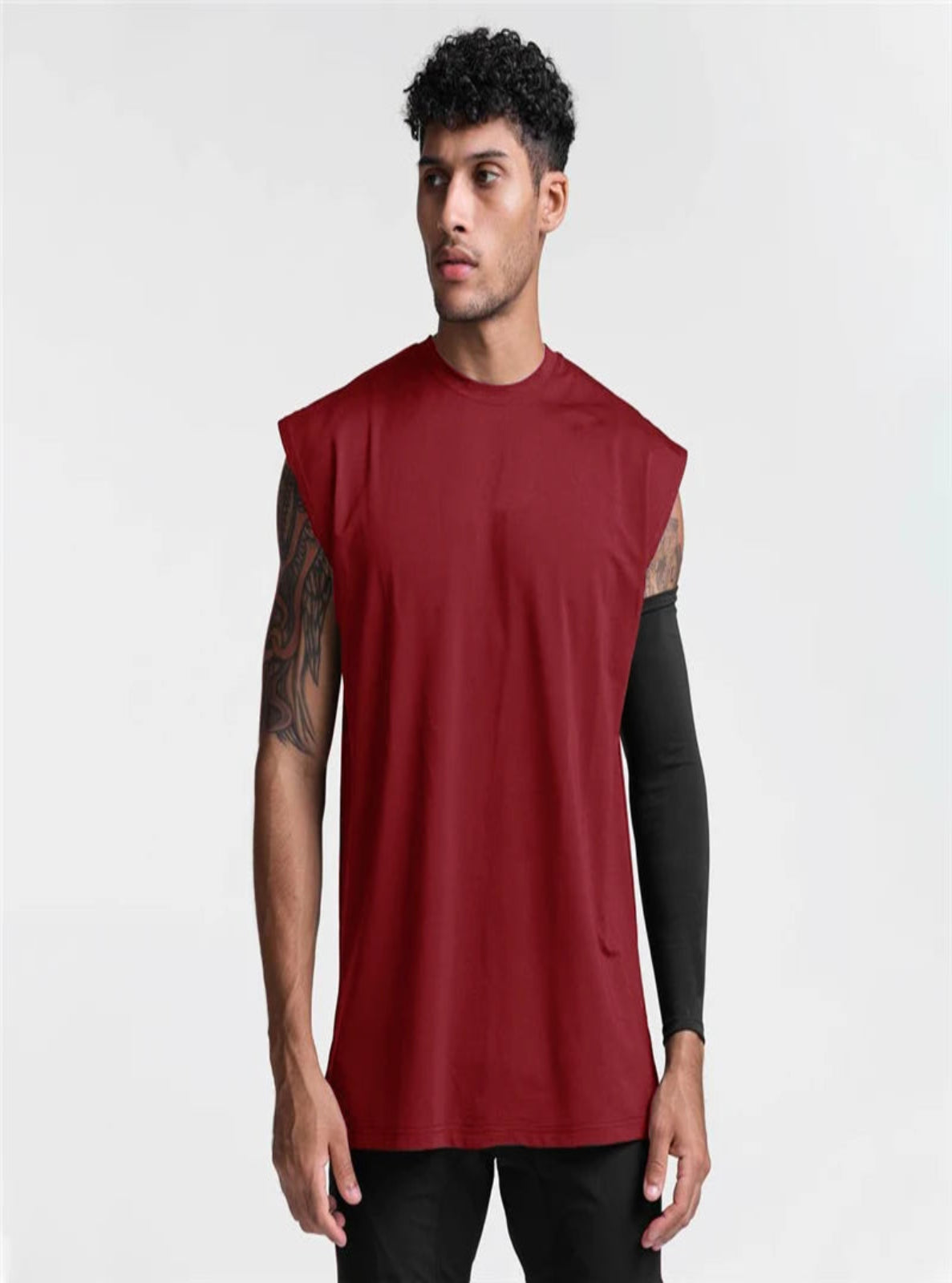 Man wearing a red sleeveless shirt with black arm sleeves on a white background