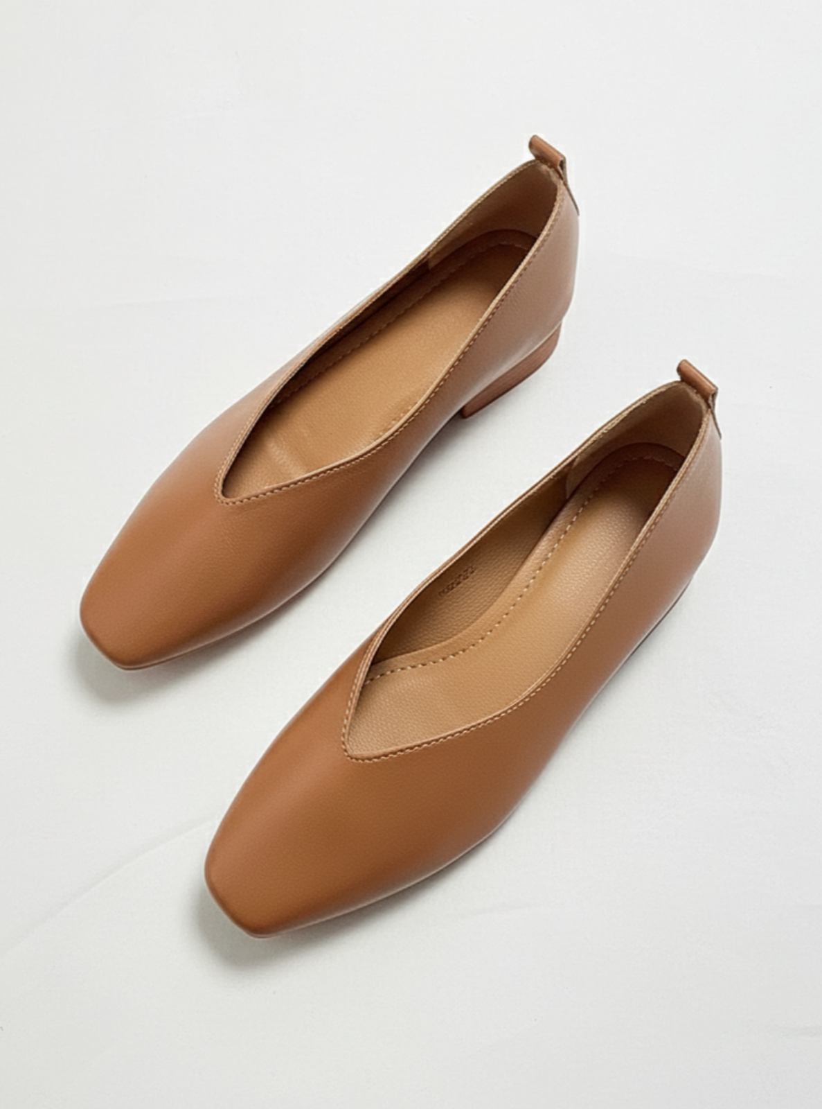 Pair of brown leather flats on a light gray background