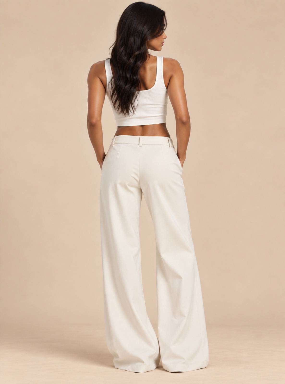 A woman shown from the back wearing a white sleeveless crop top and matching white wide-leg pants against a plain beige studio background.